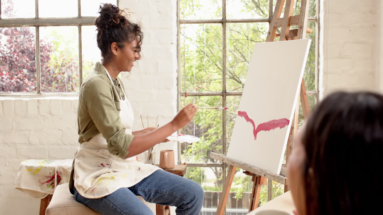 Female artist painting on canvas in bright home studio, creating abstract artwork