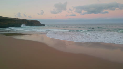 waves meet tranquil beach at dusk drone view. sunset cast warm glow over ocean