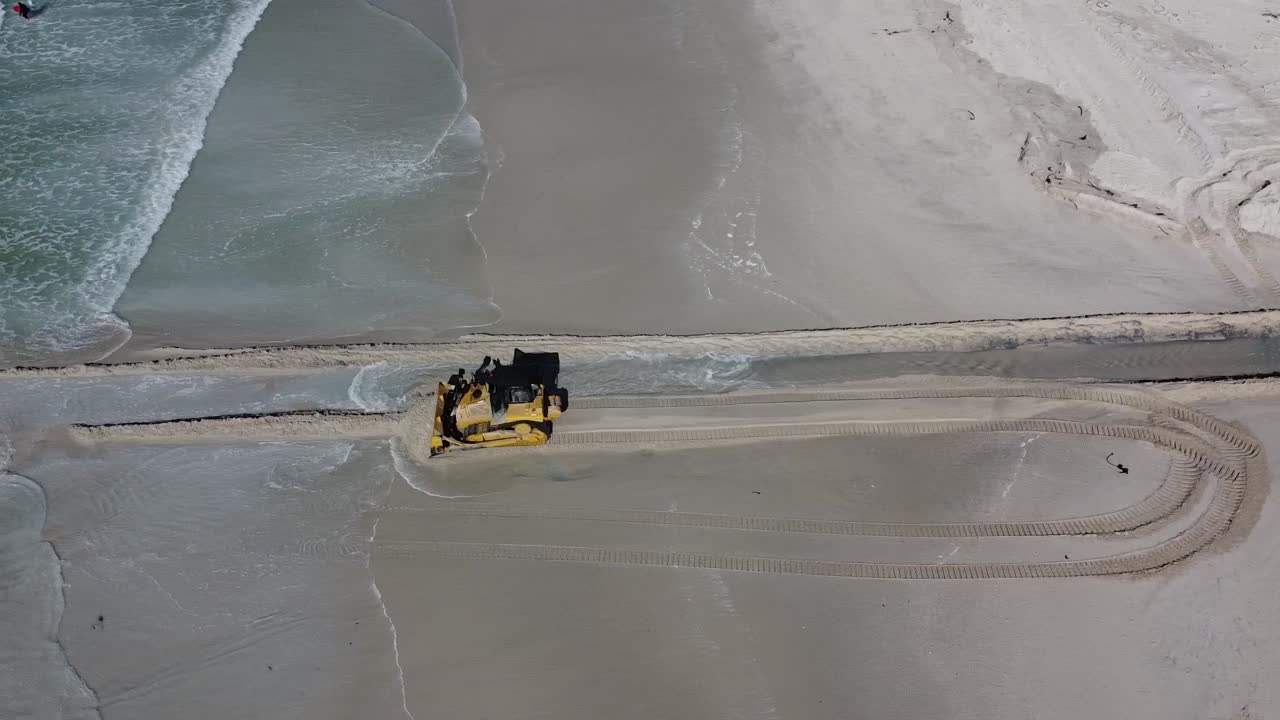 Aerial view of a bulldozer working on a sandy beach, clearing or creating a channel near the ocean