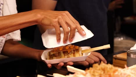 hands prepare and serve grilled skewers with sauce, using paper trays and chopsticks.