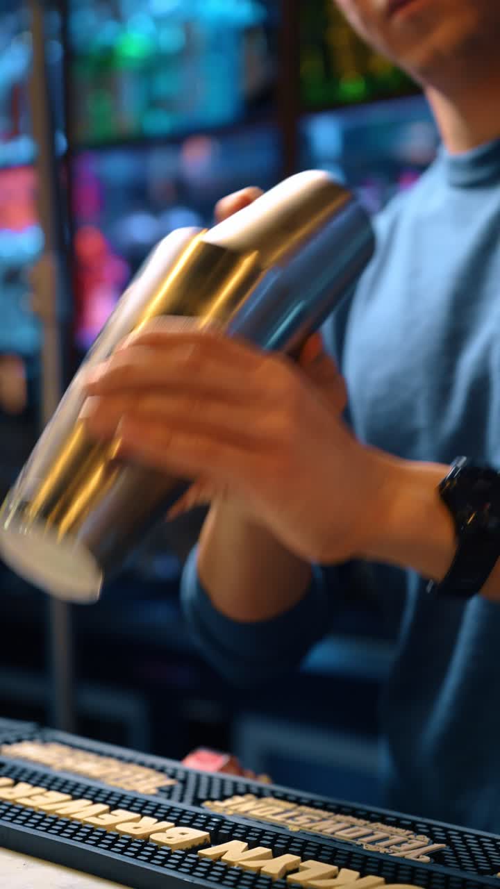 Scatto d'azione di un barman che agita uno shaker metallico per cocktail. Primo piano delle mani di un barman professionista che usa uno shaker in acciaio inossidabile al bar.