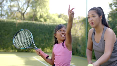 playing tennis, girl holding racket and making peace sign with woman on court