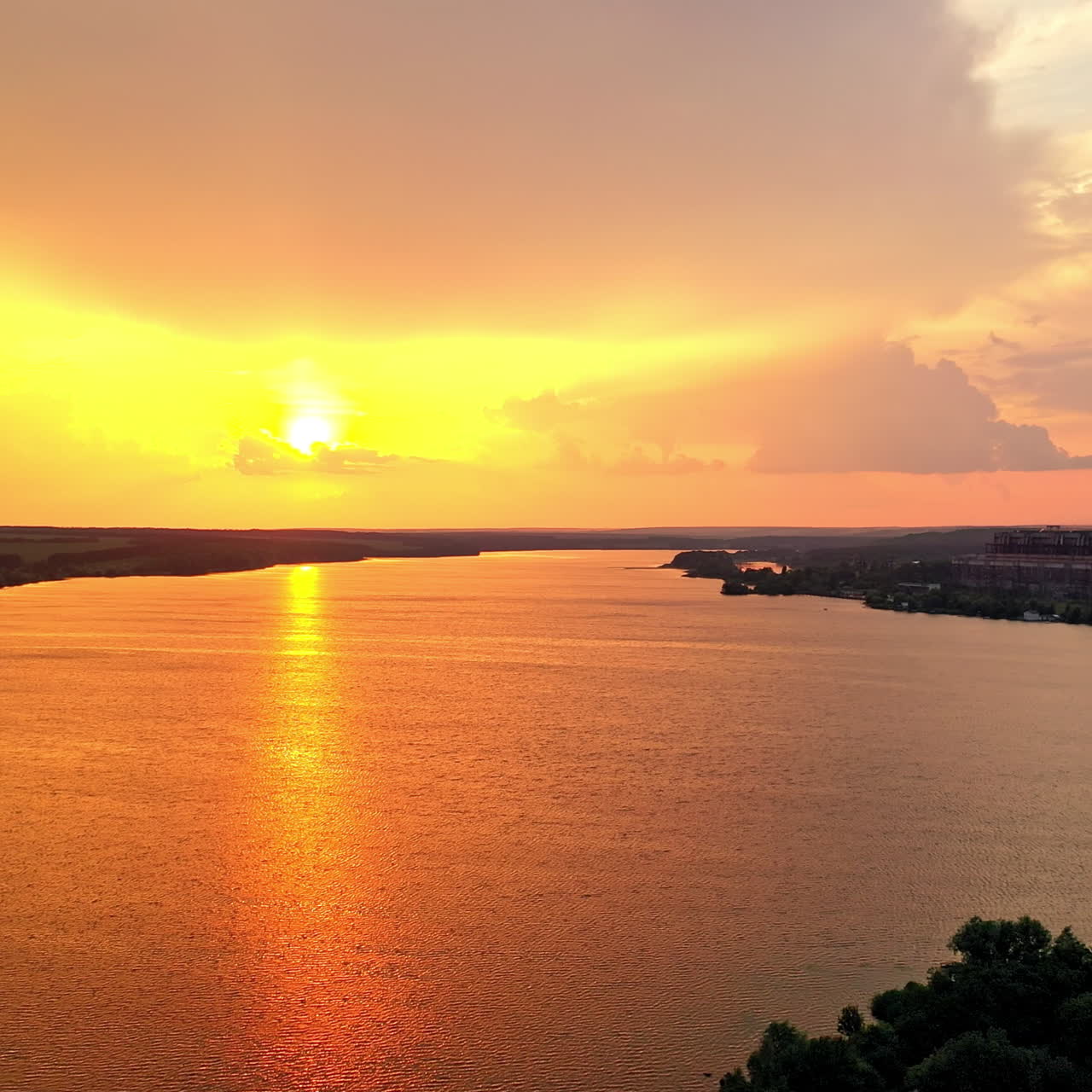 Evening view on the factory with pipes near the river. Natural scenery of the river at sunset. Golden path over the water surface. Air pollution in the environment.