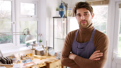 Portrait-Of-Male-Jeweller-Standing--At-Work-Bench-Working-In-Studio