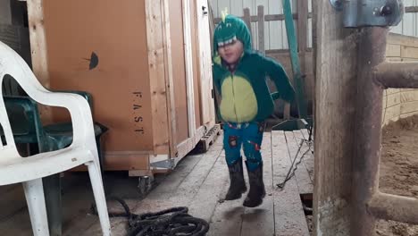 niño disfrazado de dinosaurio saltando en un granero de madera