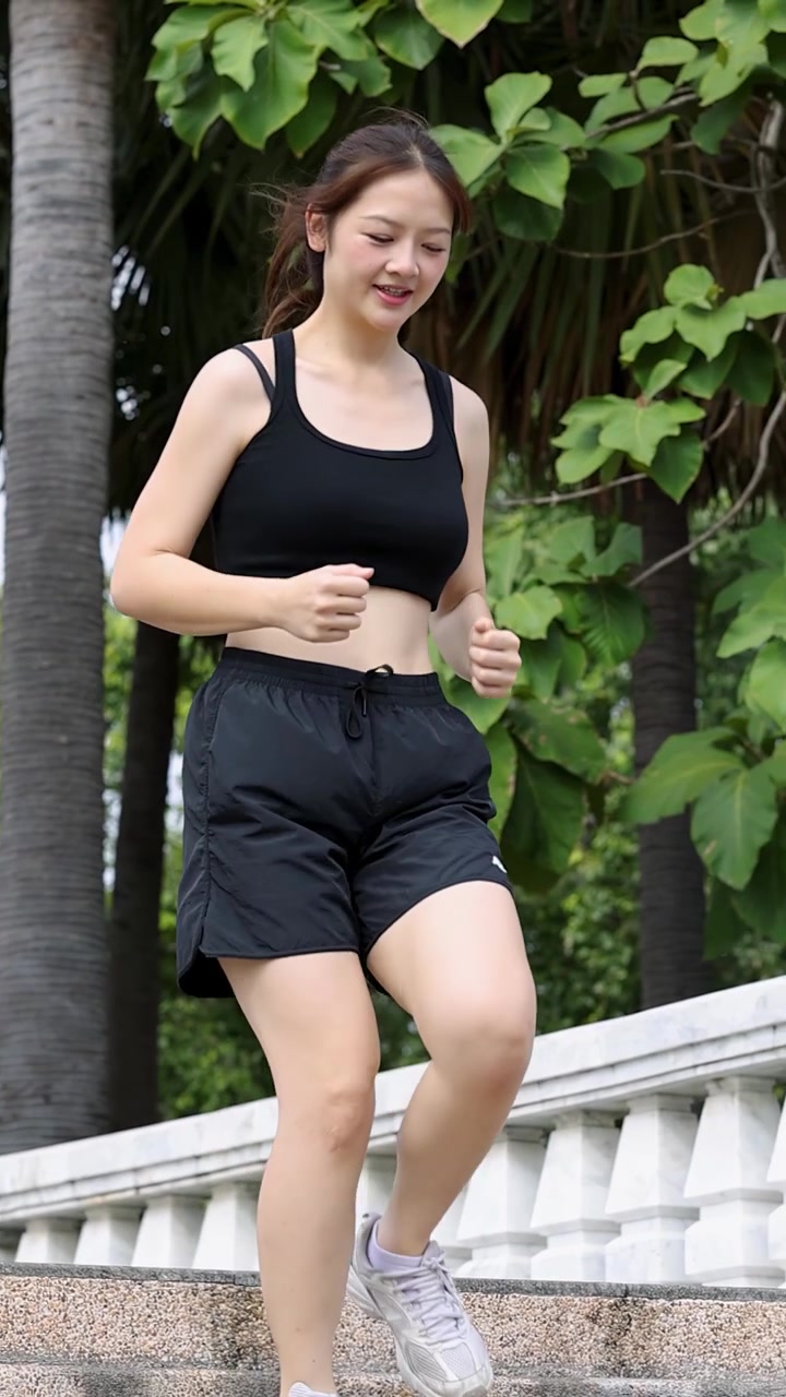 A fit Asian woman runs down stone stairs in a lush park during daytime