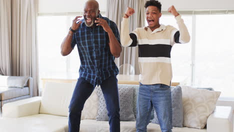 Excited-african-american-father-and-adult-son-watching-sport-on-tv-and-celebrating,-slow-motion