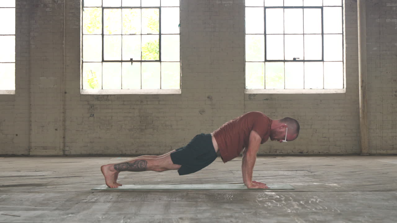 Man in an industrial warehouse practicing yoga, the pose of upward dog to downward dog.