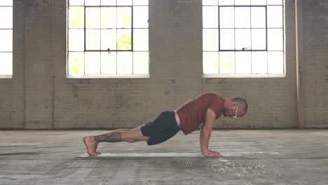 man in an industrial warehouse practicing yoga, the pose of upward dog to downward dog.