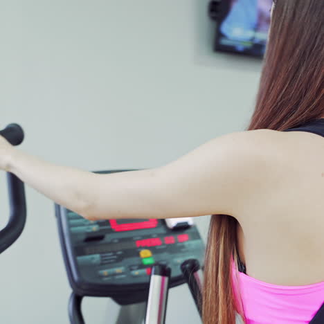 back view of the athletic body of a young pretty girl in black leggings using indoor bike. beautiful woman doing cardio workout on a cycle in fitness club. close-up