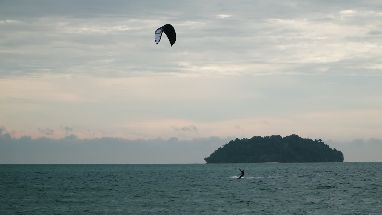 мужчина-кайтсерфер высоко прыгает во время кайтсерфинга на закате возле острова в малайзии - широкоугольный кадр слежения
