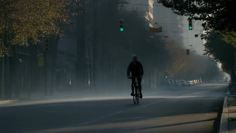 a cyclist rides on a misty urban street in the morning