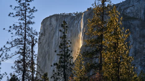 sun sets on yosemite waterfall as mist shines orange in fading sunlight