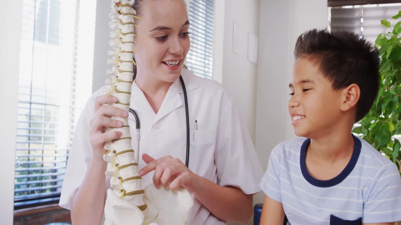 Female physiotherapist explaining spine model to boy patient 4k
