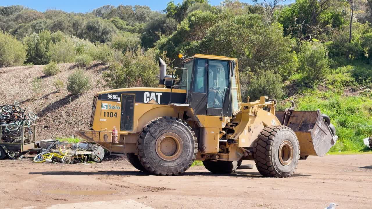 Yellow front loader dumps old tires at a sunny outdoor waste facility in Australia