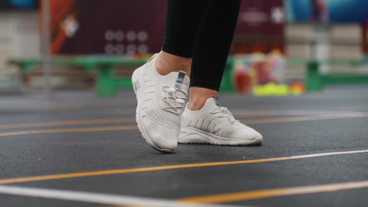 Ejercicio de precisión de juego de pies en interiores. Práctica de colocación precisa de los pies usando zapatillas deportivas blancas en interiores. Mejora de la técnica en la cancha mediante movimientos de pivote controlados en sesiones de entrenamiento de bádminton.