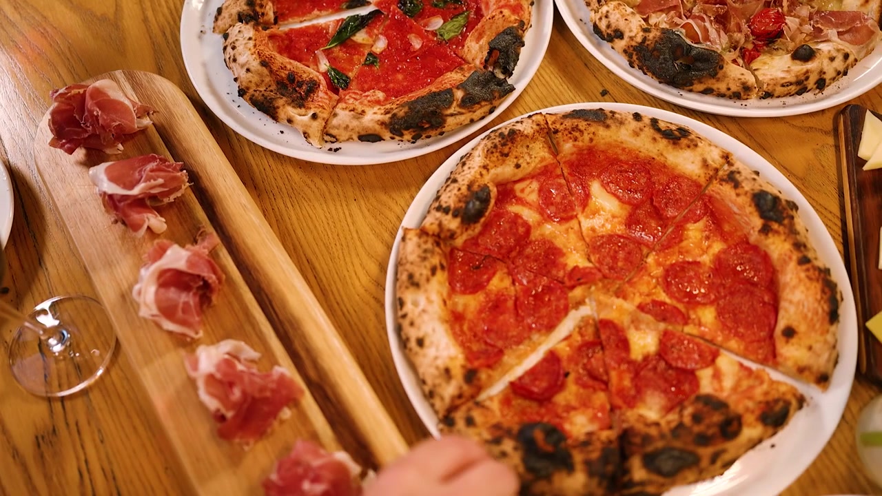 Persone che condividono pizze artigianali assortite a un tavolo di ristorante.