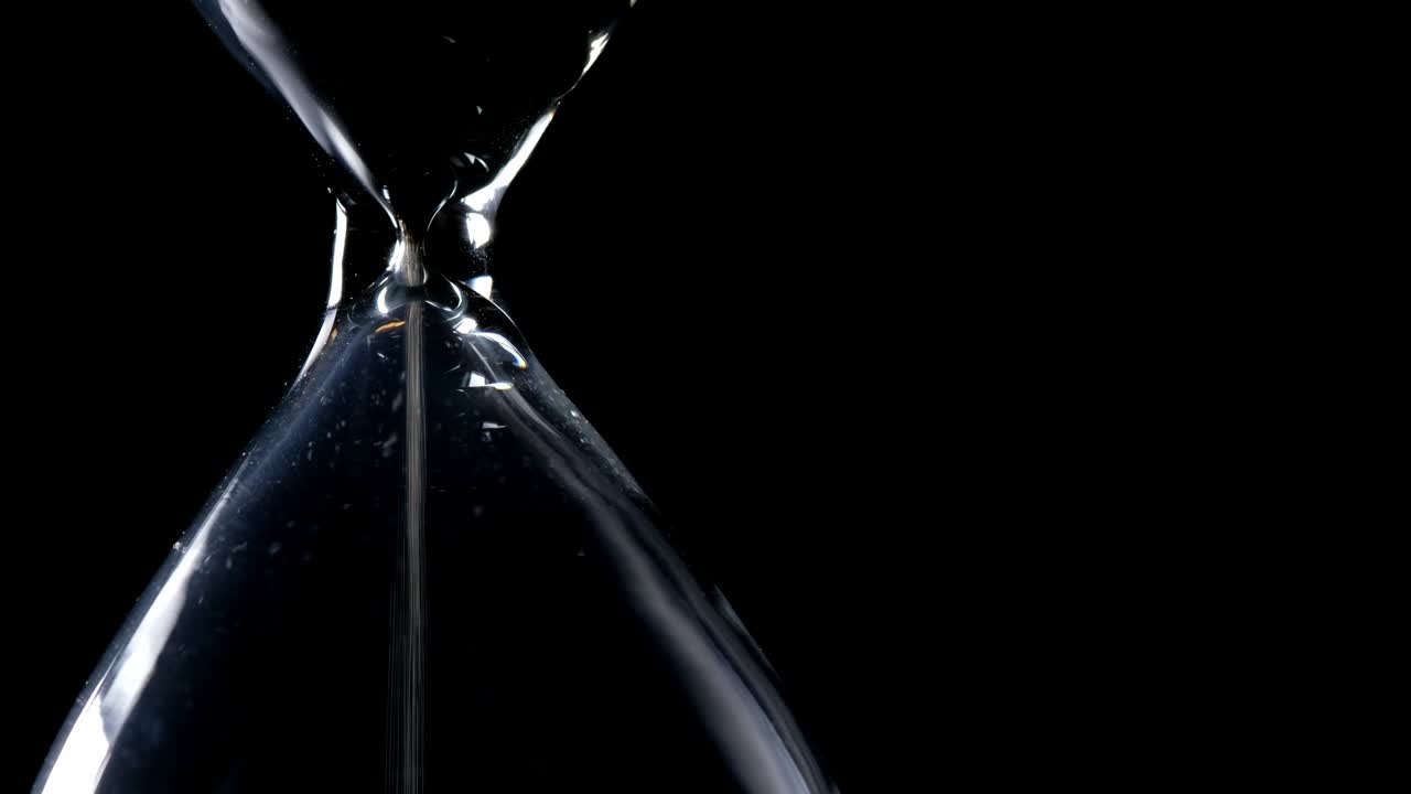 Il flusso di sabbia nella clessidra con sfondo nero e retroilluminazione a luce laterale in composizione laterale e possibile loop infinito