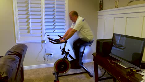 lapso de tiempo de un entrenamiento maduro de calentamiento para cardio en una bicicleta estacionaria en su casa y leyendo en una tableta - desenfoque de movimiento de larga exposición