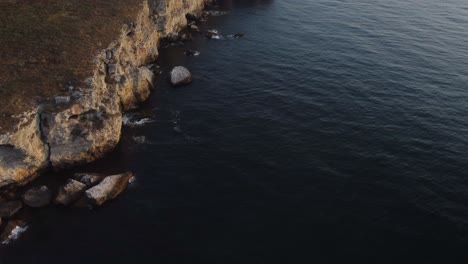 Drone-top-down-aerial-view-of-waves-splash-against-rocky-seashore,-background