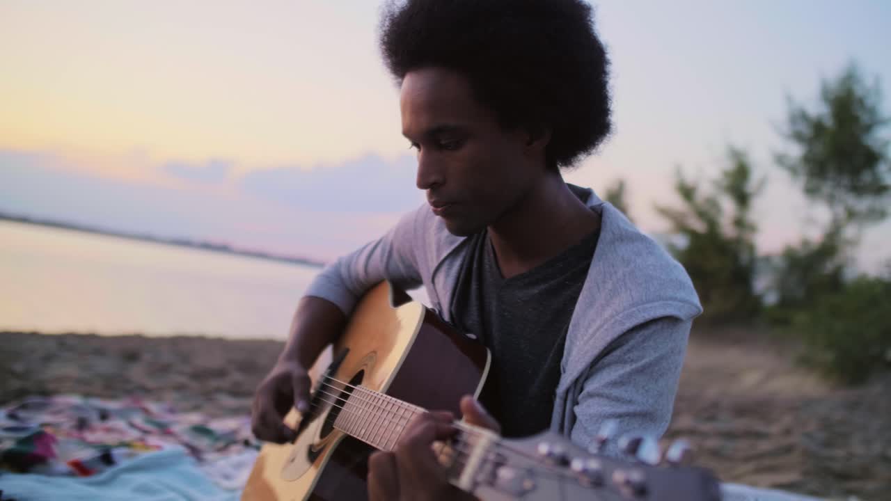 Håndholdt billede af afrikansk mand, der spiller guitar og synger på stranden/Dabrowa Gornicza/Polen