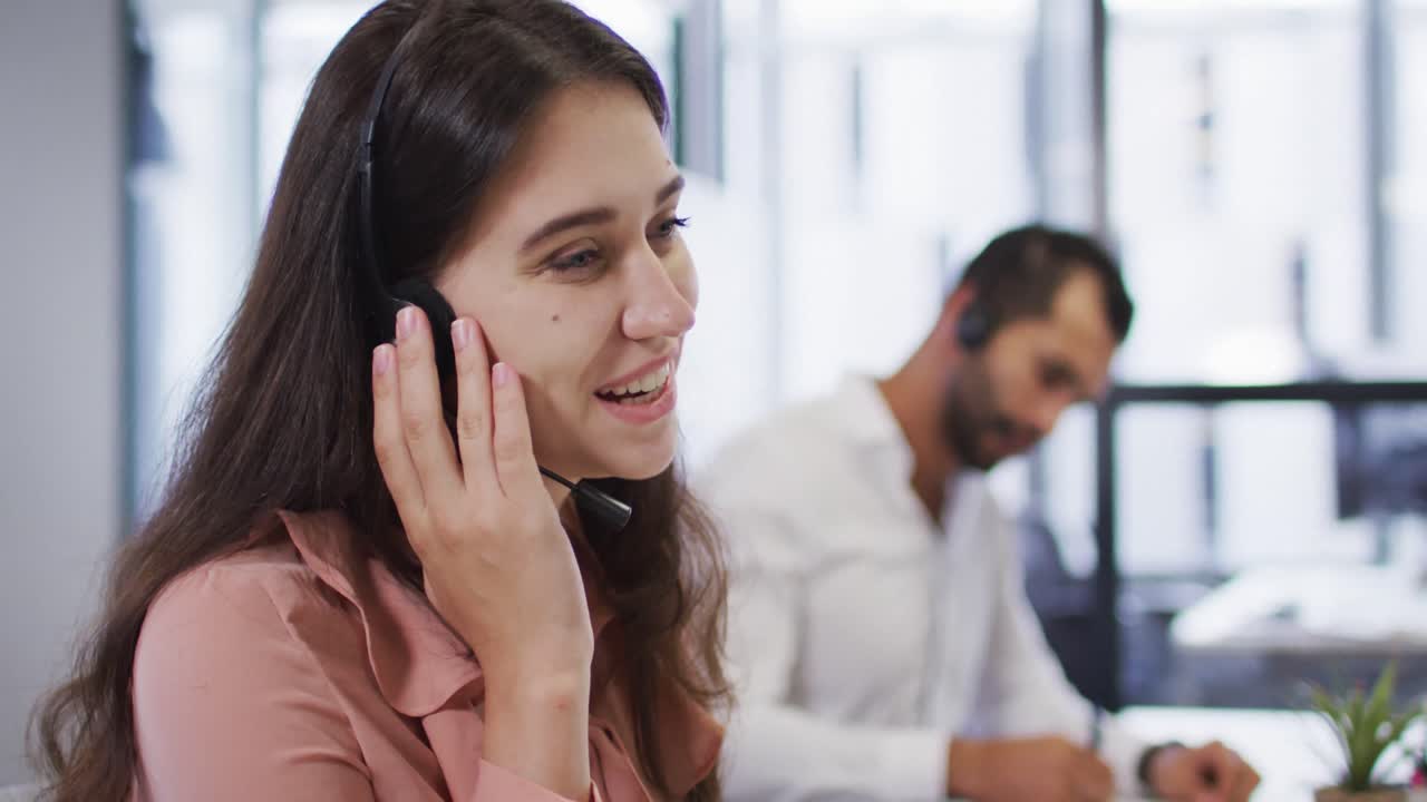 retrato de una mujer de negocios caucásica en un escritorio usando auriculares de teléfono y sonriendo a la cámara