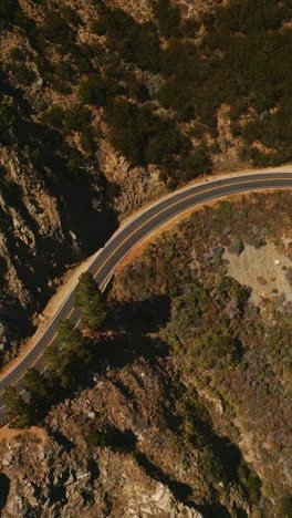 motorway passing through the huge mountain. cars moving by the dangerous road at the edge of rock. aerial view. vertical video