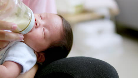 holding a baby bottle filled with formula milk to feed a sleeping baby cradled in her mother's arms