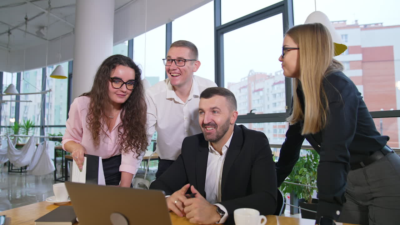 Smiley cheerful team of coworkers looking at laptop and discussing something. Boss and his employees working in a good mood.