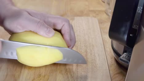 slow motion slider shot of slicing a potato on a wooden chopping board in the kitchen