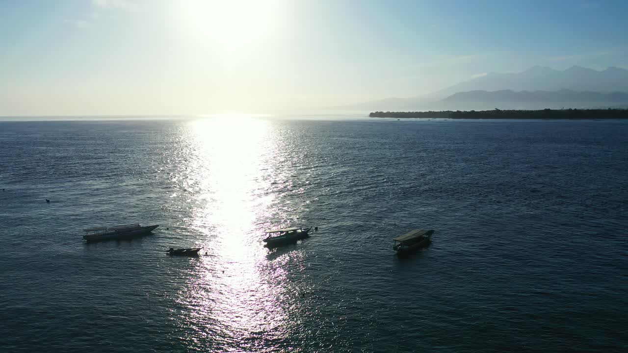Sun reflecting on the calm sea water. Tropical island on a foggy day with floating fishing boats near the coast