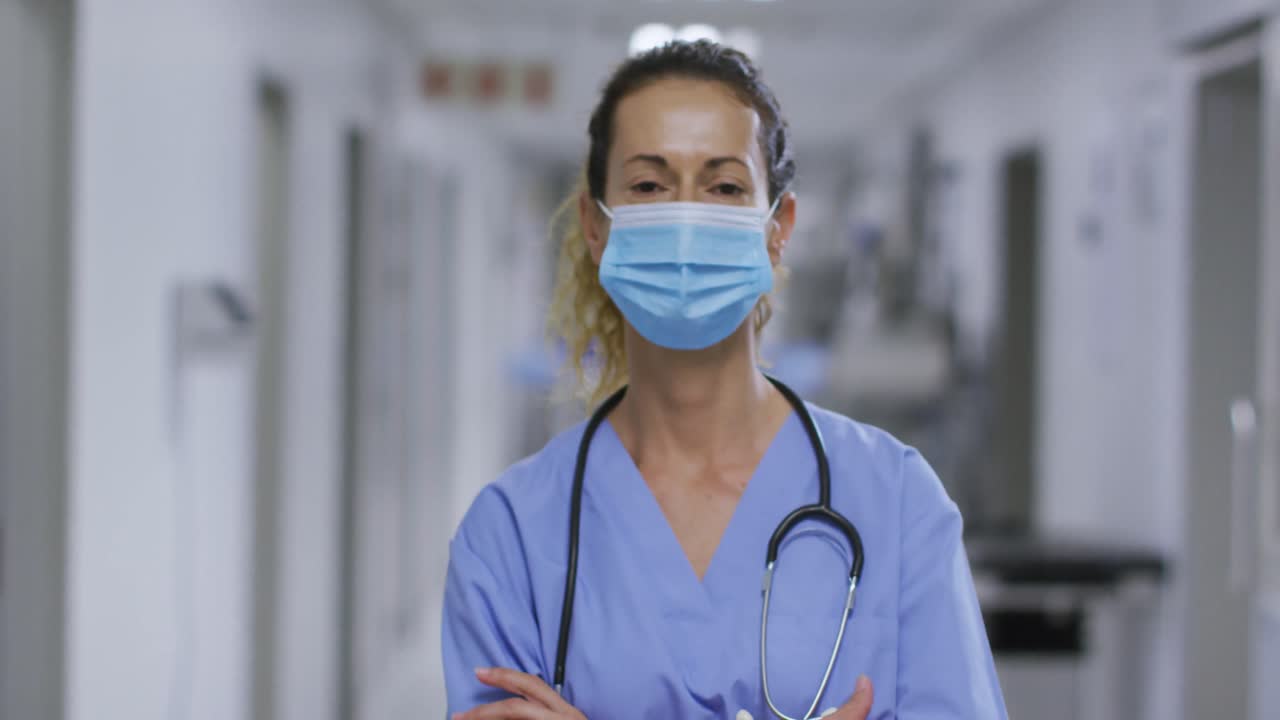 Retrato de profissional de saúde caucasiana usando máscara facial no corredor do hospital.