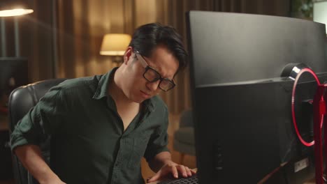 asian male paining his back while works on his personal computer, he works late at night
