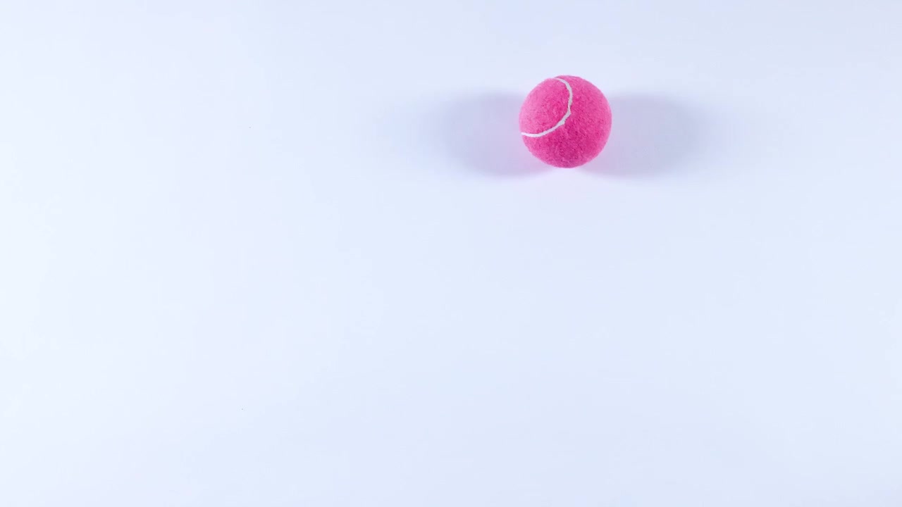 A pink tennis ball rolls across a surface