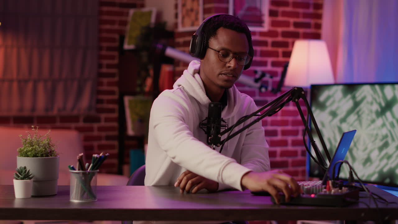 African american online radio host reading fan mail from laptop talking using microphone