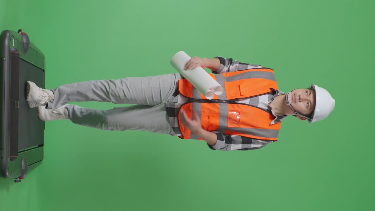 안전 헬을 입은 아시아 남성 엔지니어의 몸 전체가 손에 청사진을 들고 녹색 스크린 배경 스튜디오에서 는 동안 주위를 둘러보고 있습니다.