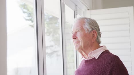 Glücklicher-Kaukasischer-älterer-Mann,-Der-Lächelt-Und-Allein-Durch-Das-Fenster-Schaut