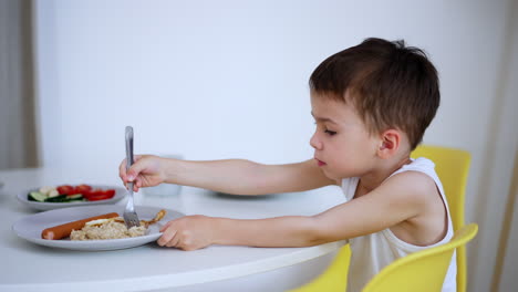 young boy enjoying a meal at home. a young boy sits at a table, happily eating a nutritious meal of rice, vegetables, and sausage