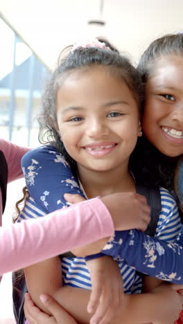 vertical video: in school, three young biracial female friends are hugging
