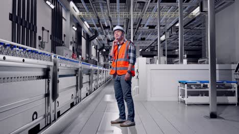 full body side view of asian male engineer with safety helmet thinking and looking around then raising his index finger while standing with water production in bottling factory