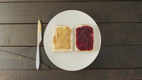 vista de cerca de mantequilla de maní y sándwich de jalea en un plato con cuchillo de mantequilla en la superficie de madera