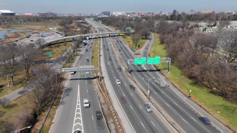 An-aerial-time-lapse-over-a-busy-highway-on-a-sunny-day-between-a-lake-and-a-graveyard-in-Queens,-New-York