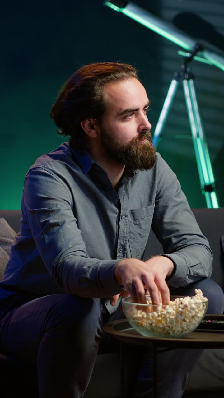 Vertical video Man at home on couch gripped by interesting film shown on television screen