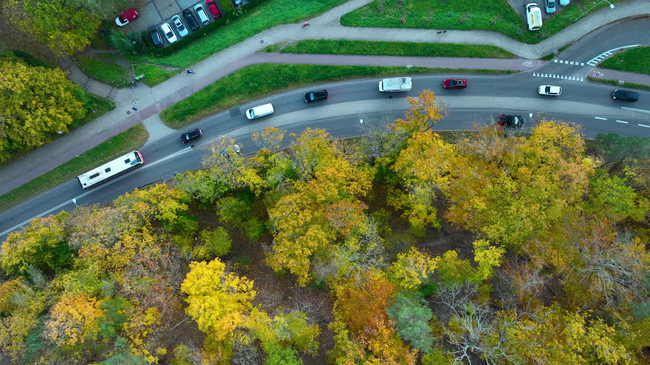 Top-down shot of a curve in the road with dense autumn forest and cars travelling in both directions