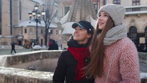 Two-smiling-women-sisters-tourists-walking-together-on-city-street,-couple-talking,-embracing