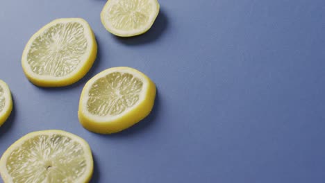 Video-of-slices-of-lemon-lying-on-blue-background-with-copy-space