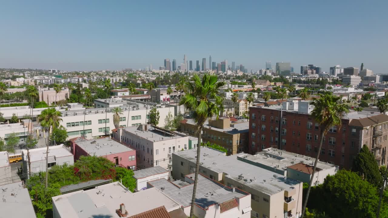 Sorvolando un quartiere fiancheggiato da palme verso lo skyline del centro di Los Angeles