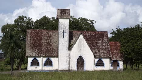 Una-Antigua-Capilla-Cristiana-Blanca-Y-Azul-Abandonada-Con-Una-Pequeña-Cruz-Tapiada-Rodeada-De-Malezas-Y-árboles-Tropicales-Al-Costado-De-Una-Carretera-En-El-Estado-De-Pernambuco-En-El-Noreste-De-Brasil