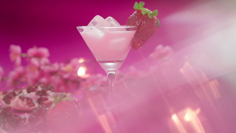 video product composition of a martini glass with a strawberry milkshake, surrounded by fresh strawberries, pomegranates and candles