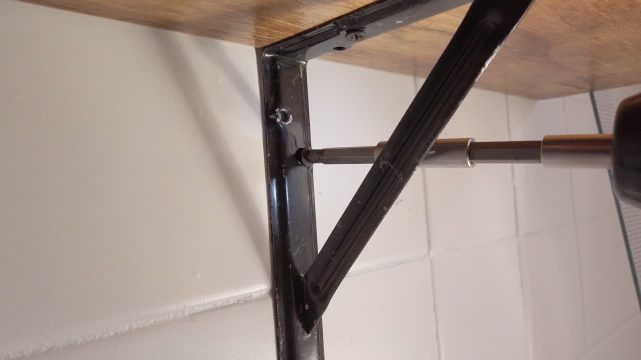 Close up of screwdriver fastening metal bracket to wall during shelf installation